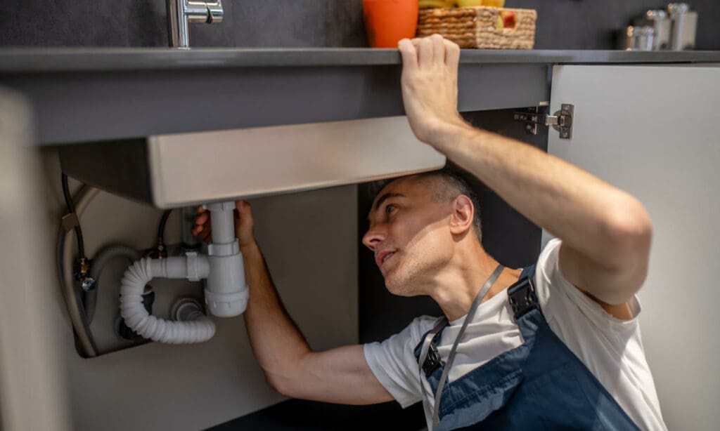 Man carefully examining bottom of sink and pipe